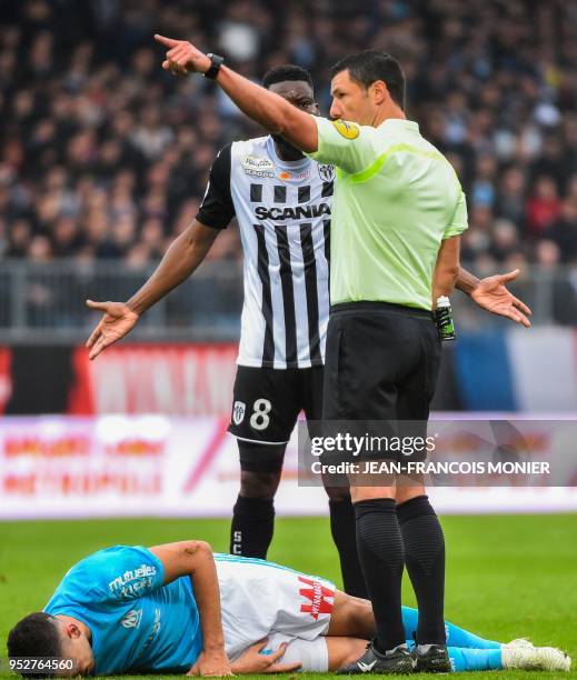 French referee Nicolas Rainville gestures as he talks to Angers' defender Ismael Traore as Marseille's Argentinian forward Lucas Ocampos lies in pain...