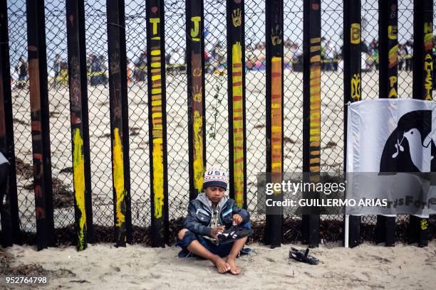 Central American migrant boy travelling in the "Migrant Via Crucis" caravan removes sand of his shoes during a demonstration at the US/Mexico Border...