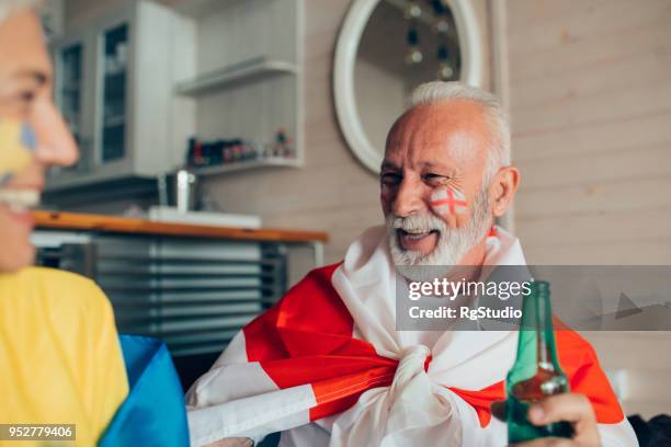 happy mature couple watching soccer game and drinking beer - england flag stock pictures, royalty-free photos & images