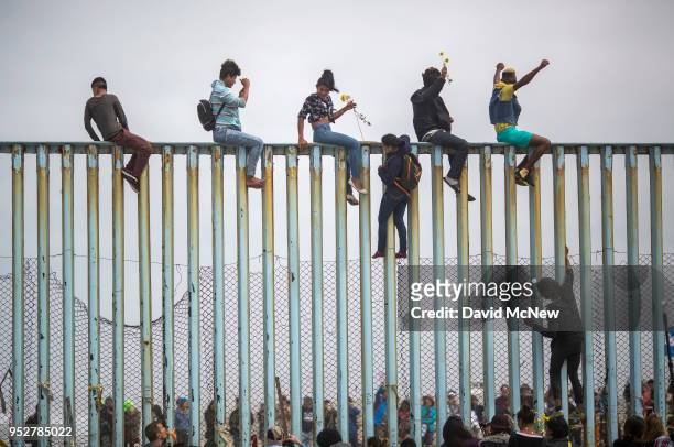 People climb a section of border fence to look toward supporters in the U.S. As members of a caravan of Central American asylum seekers arrive to a...