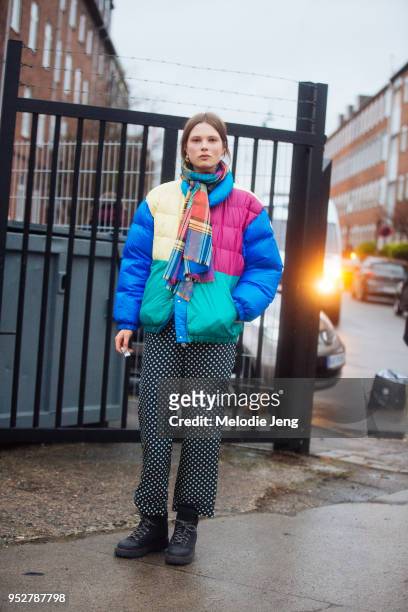 Model Caroline Brasch Nielsen wears a madras colorful scarf, a multi-color down jacket, black and white polka dot pants, and black boot sat...