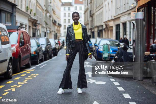Model Adut Akech wears a black leather jacket, yellow sweater, black pinstripe flare jeans, and white sneakers on January 23, 2018 in Paris, France.