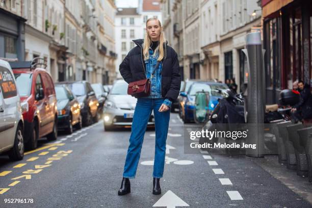 Model Jessie Bloemendaal wears a black puffer jacket, maroon purse, denim jacket and blue jeans, and black bootson January 23, 2018 in Paris, France.