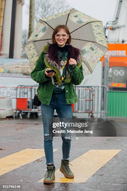 Model Fran Summers carries a Gustav Klimt umbrella, holds her phone, and wears oversized glasses, a green corduroy jacket with a fur lining, a green...