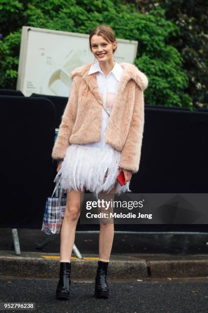 Model Kris Grikaite wears a short pink fur jacket, a white Prada Feather-trimmed cotton dress, Opening Ceremony bag, and black boots on January 23,...
