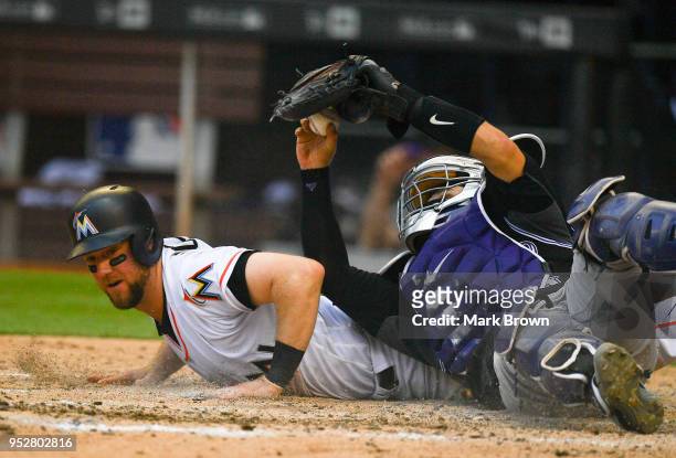 Tony Wolters of the Colorado Rockies attempts to retag Bryan Holaday of the Miami Marlins after he slid into home plate for the score in the eighth...