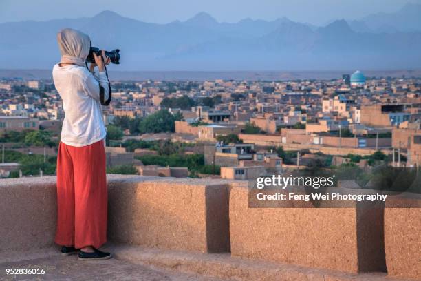 female tourist taking photos of cityscape at dusk, narin castle, meybod, yazd province, iran - yazd stockfoto's en -beelden