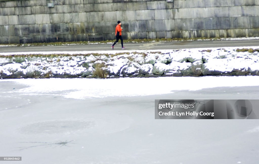 Defocused single female jogger running along riverside in snow