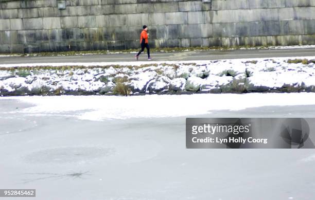 defocused single female jogger running along riverside in snow - lyn holly coorg stock pictures, royalty-free photos & images