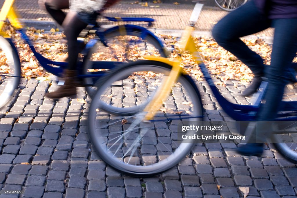 Defocused cyclists riding along Dutch cobbled street