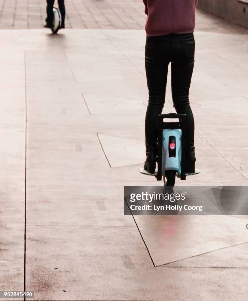 rear view of woman's legs on electric unicycle riding along sidewalk - lyn holly coorg stock-fotos und bilder