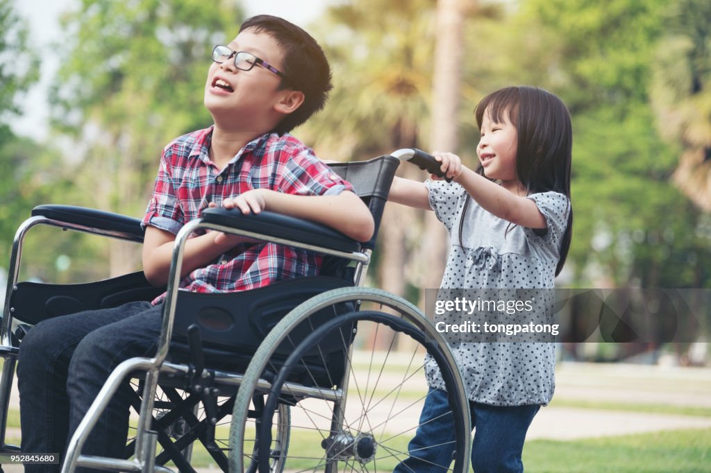 Happy boy in wheelchair with girl try drive a wheelchair of her brother smile, family time