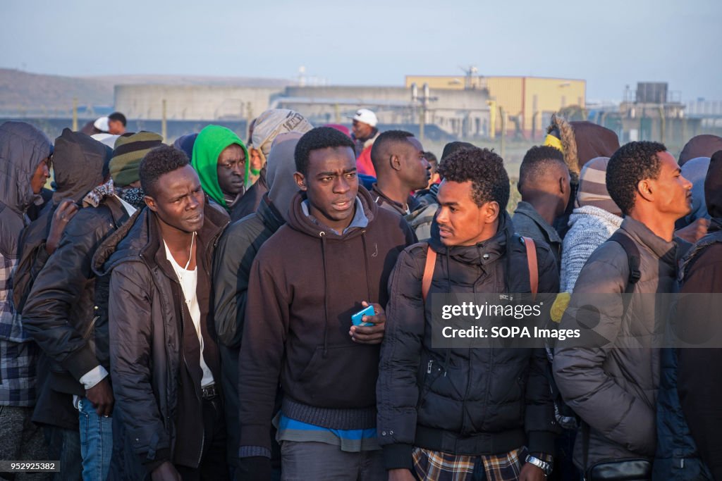 Refugees and migrants stand in line waiting to leave the...