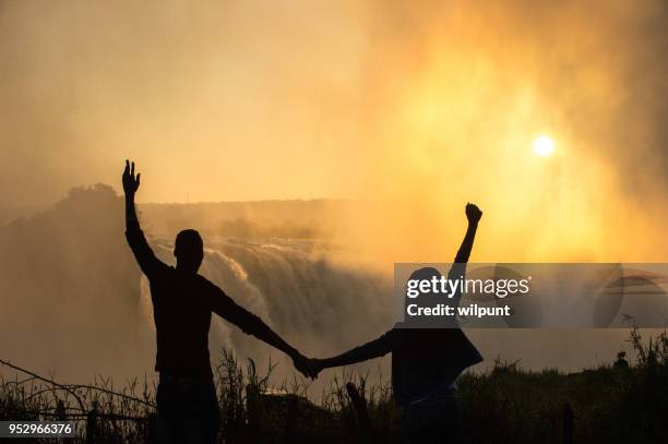 silhouette di coppia al mattino presto a victoria falls arms raised - repubblica dello zimbabwe foto e immagini stock