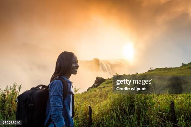 woman with backpack looking at victoria falls at sunrise - victoria falls stock pictures, royalty-free photos & images
