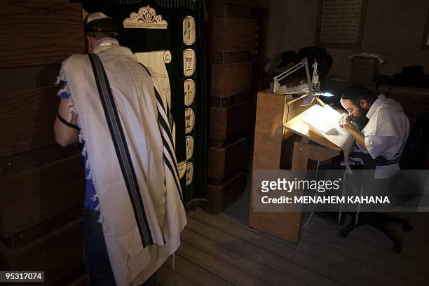 Rabbi Shai Abramovich writes a new Torah scroll as a man prays in the ancient synagogue of the hilltop fortress of Masada in the Judean desert on...