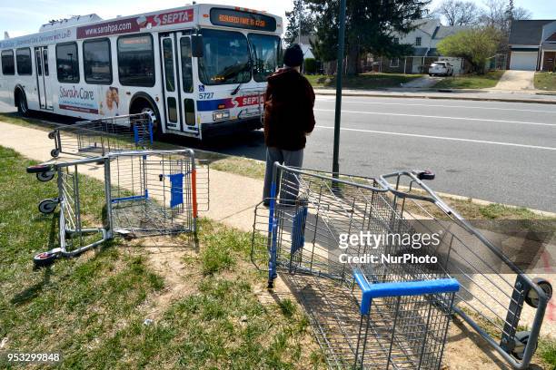 Commuters use Wallmart shopping cards as a makeshift seat while waiting for a bus, at a bus stop in NorthWest Philadelphia, PA, on April 14, 2018....