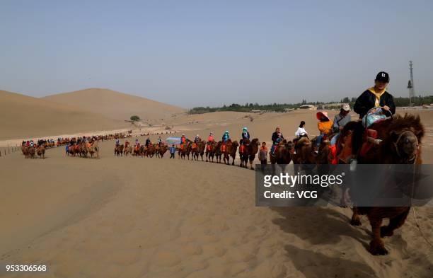 Visitors explore the sand dunes by camels on the desert of Mingsha Mountain on the second day of the 3-day International Workers' Day holiday on...