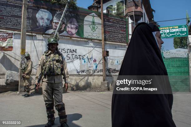 Burqa clad woman walks past as Indian paramilitary troops stands alert during restrictions in Downtown area of Srinagar city, summer capital of Jammu...