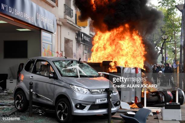 People look at a fire burning down a car and a motorbike during a demonstration on the side lines of the march for the annual May Day workers' rally,...