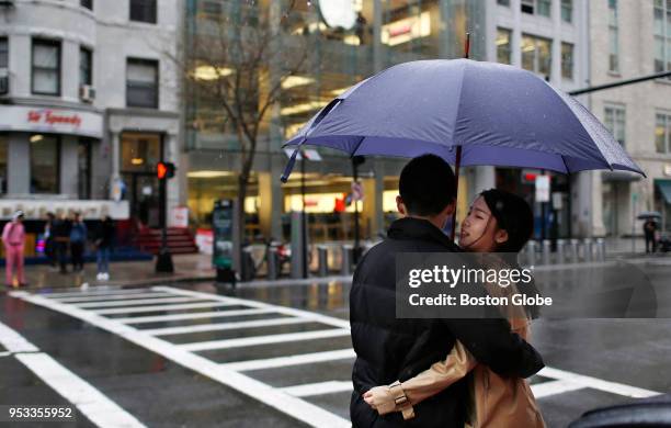 Couple embraces under an umbrella as they wait to cross Boylston Street on a rainy day in Boston, April 30, 2018.