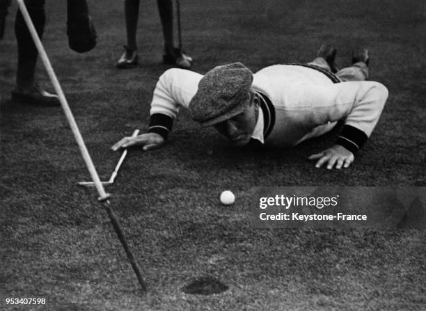 Ex boxeur Georges Carpentier, sur le green, est allongé sur l'herbe regardant la balle de golf se dirigeant vers le trou, à Stoke Poges, Royaume-Uni...