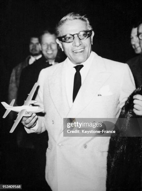 Aristote Onassis, tout sourire, tient dans ses mains un avion miniature à son arrivée à Londres, Royaume-Uni le 5 décembre 1959.