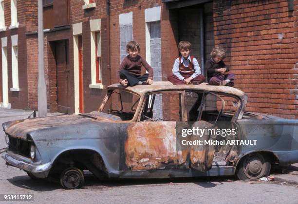 Enafnts jouant sur le toit d'une voiture brulée dans le quartier protestant de Belfast en mai 1974, Royaume-Uni.