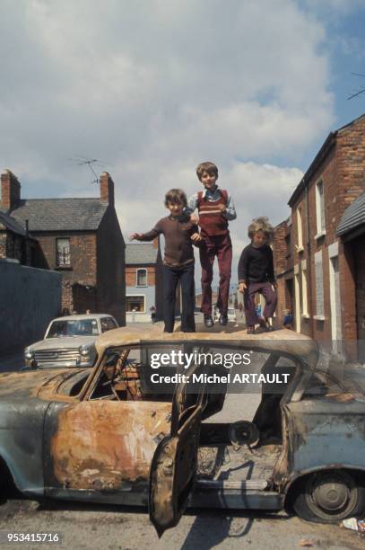 Enafnts jouant sur le toit d'une voiture brulée dans le quartier protestant de Belfast en mai 1974, Royaume-Uni.