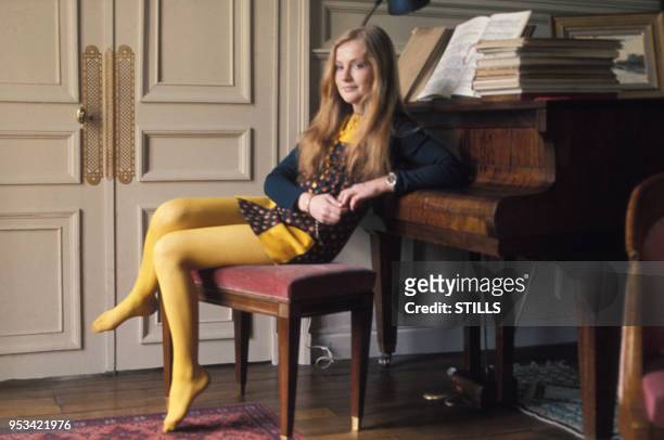 Portrait de la comédienne Isabelle Huppert portant des collants jaunes dans un salon devant un piano, circa 1970.