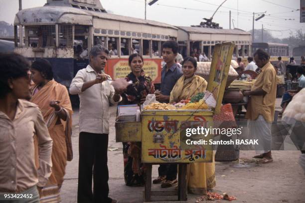 Des Indiens discutent dans la rue devant un marchand ambulant devant le passage du tramway en mai 1985 à Calcutta, Inde.