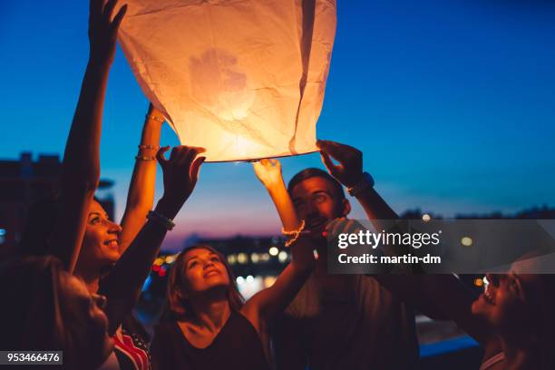 amici alla festa sul tetto che rilasciano lanterna di carta - releasing foto e immagini stock