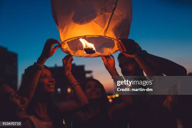 friends on rooftop party releasing paper lantern - releasing lanterns stock pictures, royalty-free photos & images