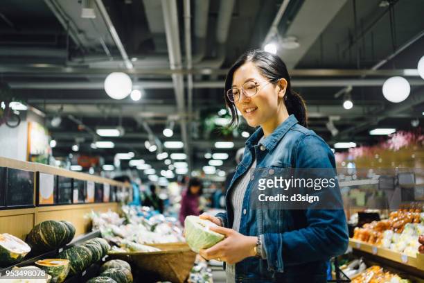 young asian woman shopping for fresh organic vegetables in supermarket - asian woman shopping grocery stock pictures, royalty-free photos & images