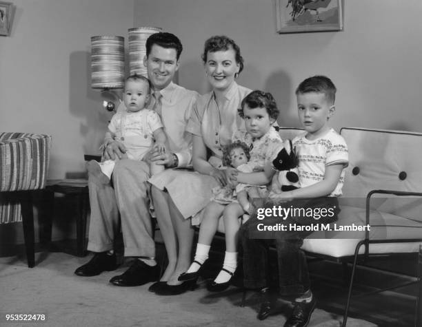 PORTRAIT OF FAMILY SITTING ON SOFA IN LIVING ROOM