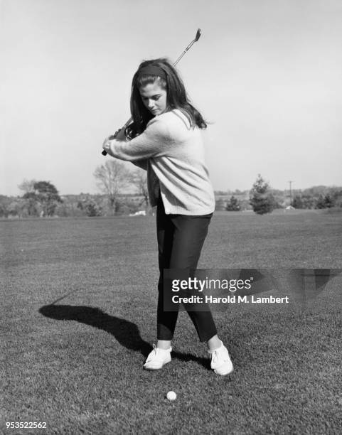 YOUNG WOMAN PLAYING GOLF AT GOLF COURSE