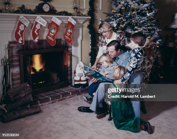 FATHER READING CHRISTMAS BOOK FOR FAMILY NEAR FIREPLACE