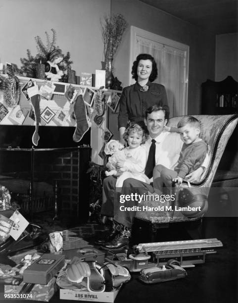 FAMILY SITTING IN LIVING ROOM NEXT TO FIREPLACE IN CHRISTMAS