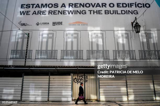 Man walks past a building that is undergoing refurbishment at Rossio Square in downtown Lisbon on April 19, 2018. - Lisbon's azure skies are dotted...