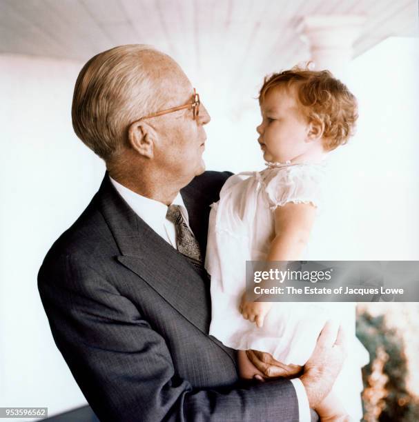 View of American businessman Joseph P Kennedy Sr as he holds his granddaughter, Caroline, on the porch of his home, Hyannis Port, Massachusetts, late...