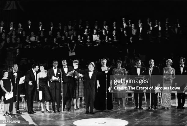 With various celebrities behind him, American entertainer Frank Sinatra raises his arms as they all perform during an Inaugural Gala in honor of John...