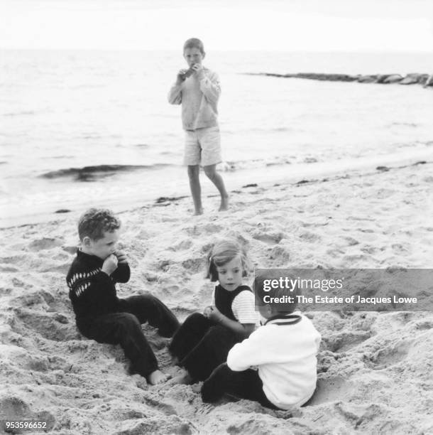 View of cousins Stephen Smith Jr , Caroline Kennedy, and Michael LeMoyne Kennedy as they sit on the sand at the beach, Hyannis Port, Massachusetts,...