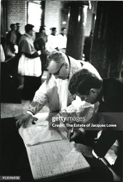 At Westminster Cathedral, English priest Gordon Wheeler watches as US President John F Kennedy signs the registry, London, England, June 5, 1961....
