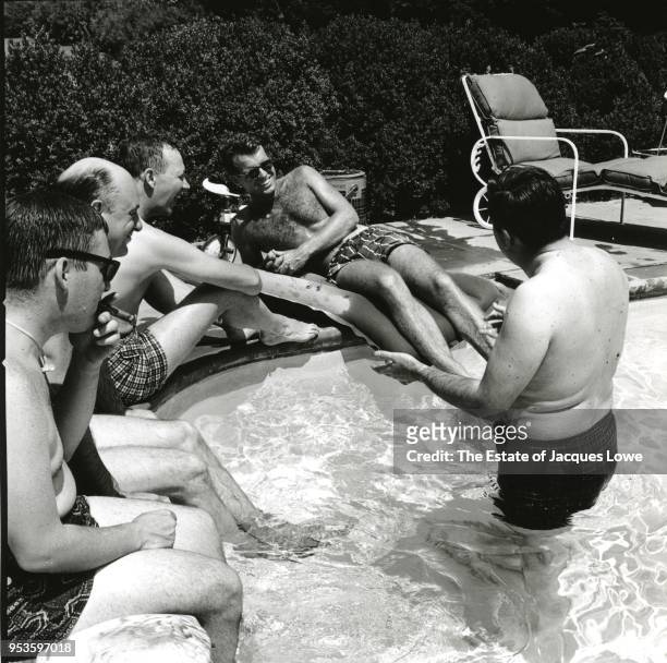 View of Robert F Kennedy as he laughs with unidentified others around the edge of a pool, late 1950s or 1960s.