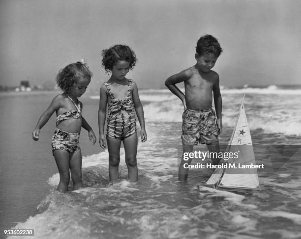 GIRLS AND BOY PLAYING WITH TOY BOAT IN SEA