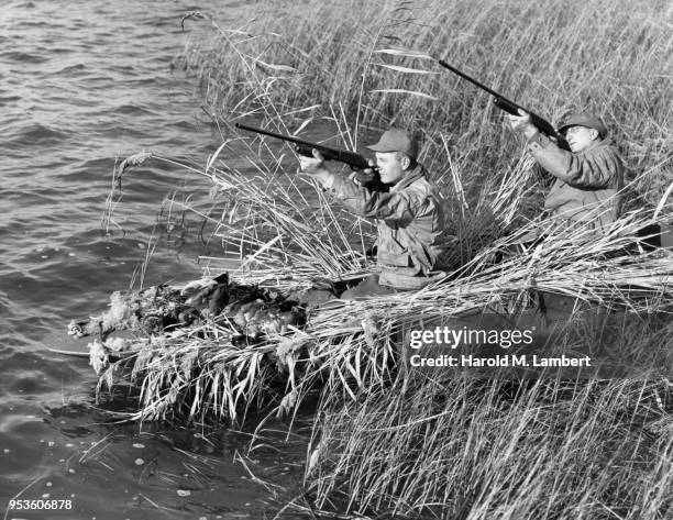 DUCK HUNTERS AIMING WITH RIFLE WHILE SITTING IN BOAT