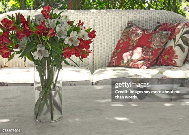outside patio with sofa, cushions and flowers over a marble coffee table. - a woman modelling a trouser suit blends in with a matching background of floral print cushions stockfoto's en -beelden