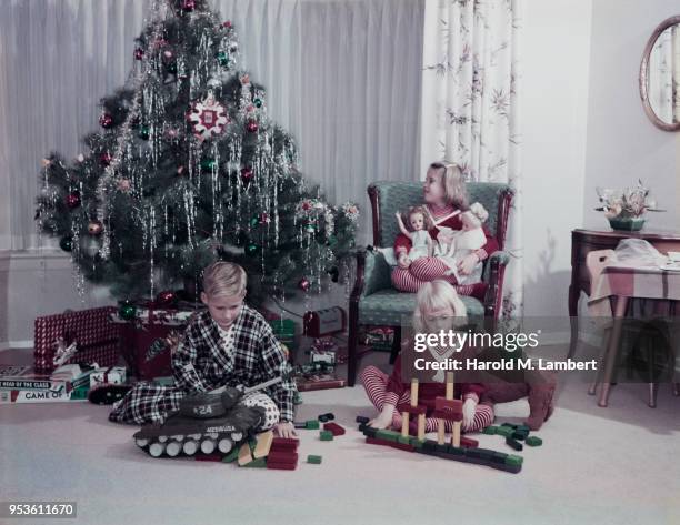 CHILDREN PLAYING WITH TOYS IN FRONT OF CHRISTMAS TREE