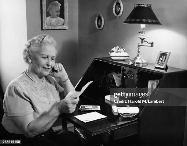 SENIOR WOMAN SITTING AT DESK READING LETTER