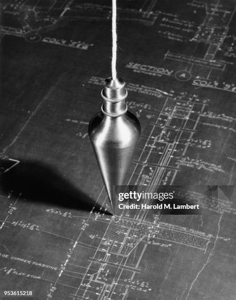 CLOSE-UP OF PLUMB BOB MEASURING TOOL OVER BLUEPRINT
